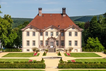 Schieder_Schloss_0024_RHa.jpg Vor einem bewaldeten Hügel erhebt sich ein elegantes Herrenhaus mit symmetrischer Gartenanlage.