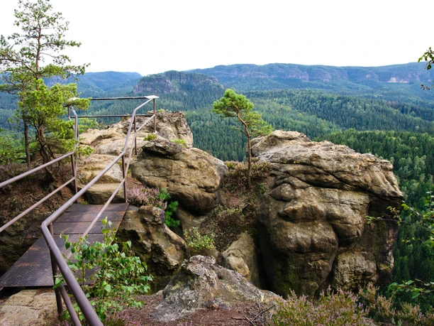 Großstein (Large stone) Metal railing on a rocky outcrop with a view of wooded hills; a single tree grows out of the rock, peaceful atmosphere.