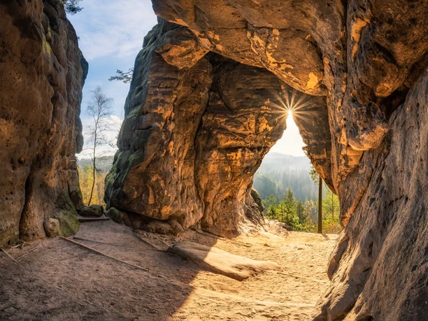 Kleinstein Cave Rock arch of the Kleinstein Cave with a view of a sunny forest, the sun shining through the opening, warm colors and a calm, natural atmosphere.