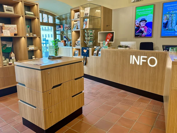 Bright information desk with wooden shelves, brochures and a bright "INFO" sign, two posters on the wall, friendly atmosphere.