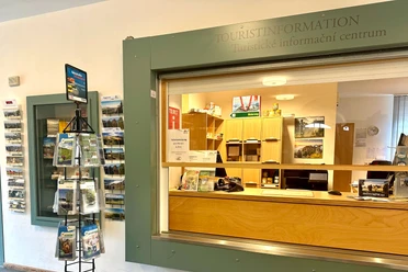 Ontmoetingsplaats Königstein Toeristische informatie met balie en brochurestand; lichtgekleurd houten meubilair, informatiemateriaal en een bord voor toiletgebruik zijn zichtbaar.