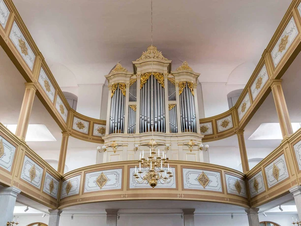 Prachtig kerkorgel met gouden versieringen in een lichte ruimte, omgeven door een galerij met twee verdiepingen en decoratieve panelen.