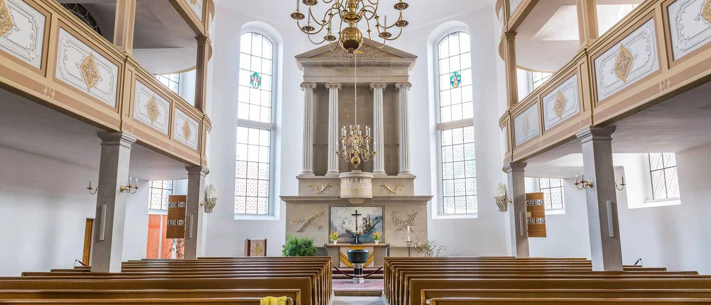 Stadtkirche Königstein Interior view of a church with wooden benches, an altar with a cross and a large chandelier; bright, calm atmosphere.