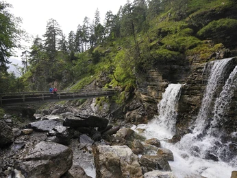 Kuhfluchtwasserfälle Farchant große Steine, eine Brücke mit 1 Person sowie 3 Wasserfälle, die rechts herunterkommen