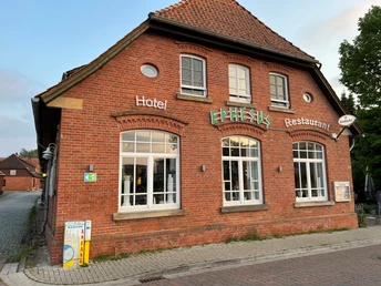 Backsteinfassade eines Hotels und Restaurants mit großen Fenstern und einem grünen Schild "Ephesus".