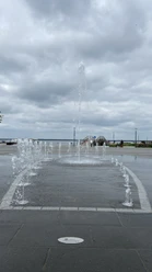 Gesamtansicht Wasserspiel_Strandterrassen Springbrunnen und Strandterrassen am Seeufer, im Hintergrund bewölkter Himmel.