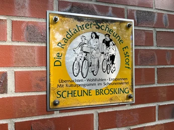 Metallschild an einer Ziegelwand mit Bild von Familie auf Fahrrädern und Text: Radfahrerscheune Estorf.