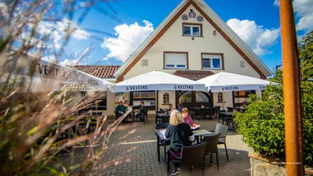 Biergarten.jpg Gäste sitzen unter weißen Sonnenschirmen im Außenbereich eines Restaurants bei sonnigem Wetter.