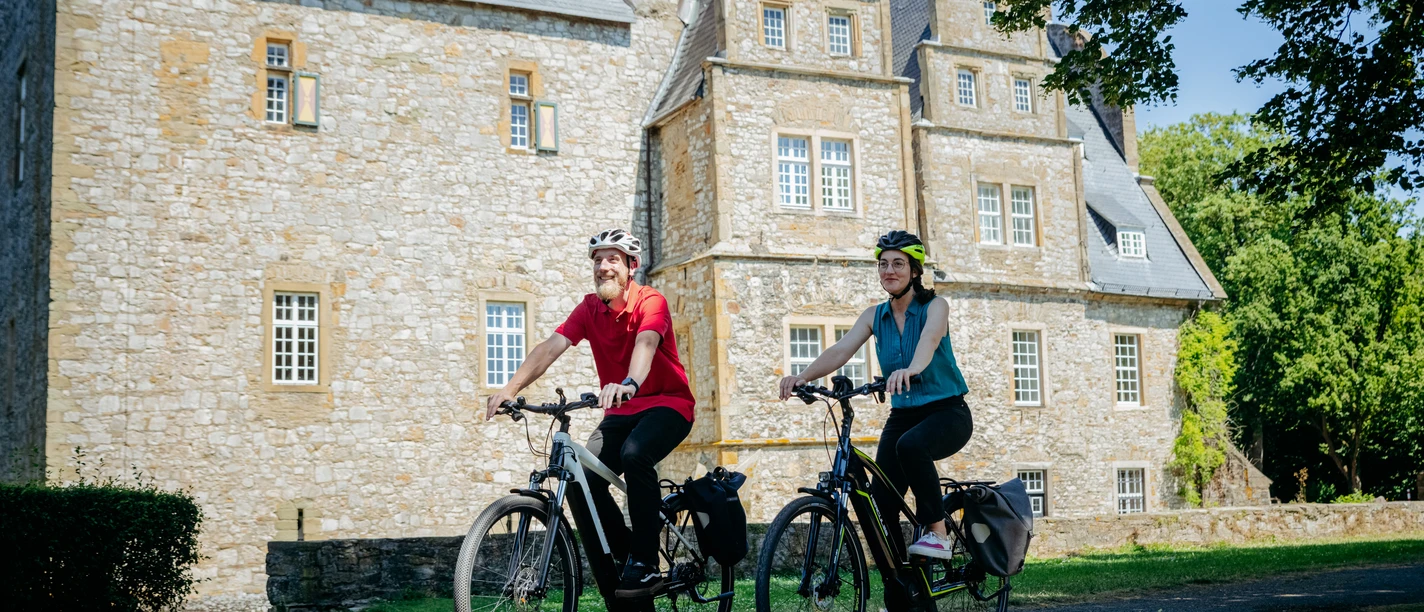 Die Schelenburg bei Bissendorf To cyklister foran en historisk herregård af sten i solskinsvejr.