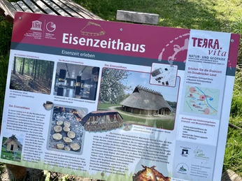 Infotafel am Eisenzeithaus Infotafel des "Eisenzeithauses" im GeoPark TERRA.vita zeigt verschiedene historische Szenen.