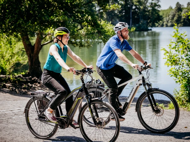 Rubbenbruchsee Two cyclists wearing safety helmets ride happily along a sunny path beside a lake.