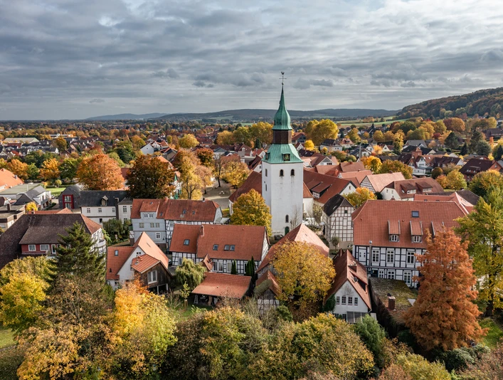 Bad Essen im Osnabrücker Land Luftaufnahme eines Dorfes mit historischem Kirchturm, Fachwerkhäusern und herbstlichem Laub.Aerial view of a village with historic church tower, half-timbered houses and autumn foliage.Luftfoto af en landsby med historisk kirketårn, bindingsværkshuse og efterårsløv.Luchtfoto van een dorp met historische kerktoren, vakwerkhuizen en herfstbladeren.