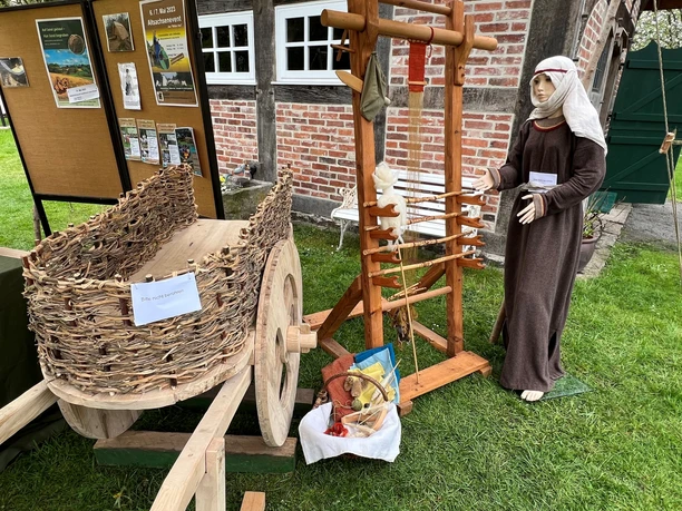 Traditionelle Webkunst auf einem Altsachsenfest mit historischem Handwagen und Gewandträgerin.