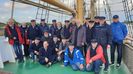 Shanty Chor Dümmer See Eine Gruppe freundlicher Männer im einheitlichen Marineoutfit steht auf einem historischen Segelschiff.