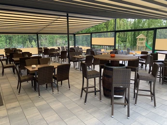 Moderne Terrasse mit Korbmöbeln und Barhockern, umgeben von Glasscheiben, spielender Kinderrutsche.