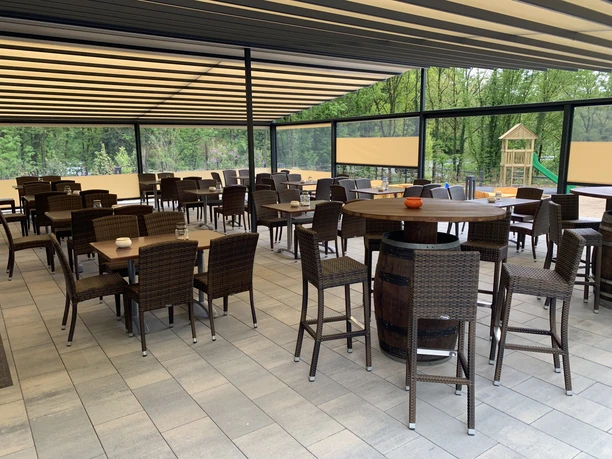 Moderne Terrasse mit Korbmöbeln und Barhockern, umgeben von Glasscheiben, spielender Kinderrutsche.