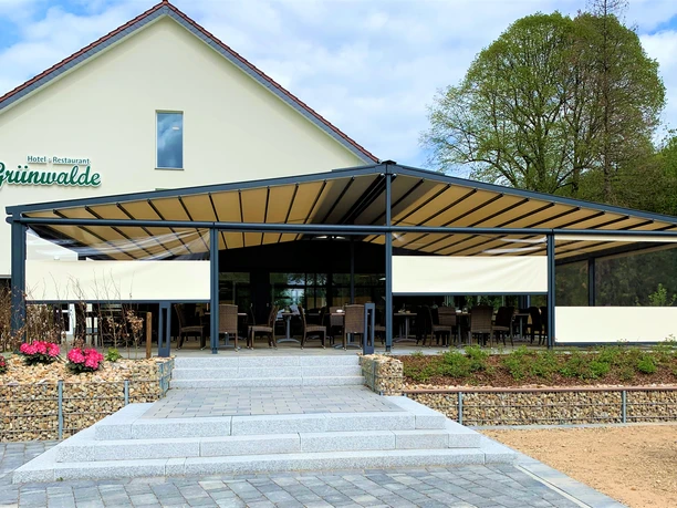 Helles Restaurant mit überdachter Terrasse und gemütlicher Bestuhlung, umgeben von blühenden Blumen.