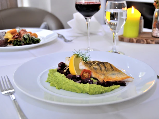 Halle-Essen-TeutoburgerWald-HotelRestaurantGrünwalde.jpg Ein Gourmetteller mit saftigem Fischfilet auf Erbsenpüree, garniert mit Gemüse und Zitronenscheiben.