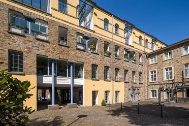 Außenansicht Kraftwerk Gelbes und steinernes Gebäude mit Arkaden, Fenstern und künstlerischen Außenskulpturen im Innenhof.