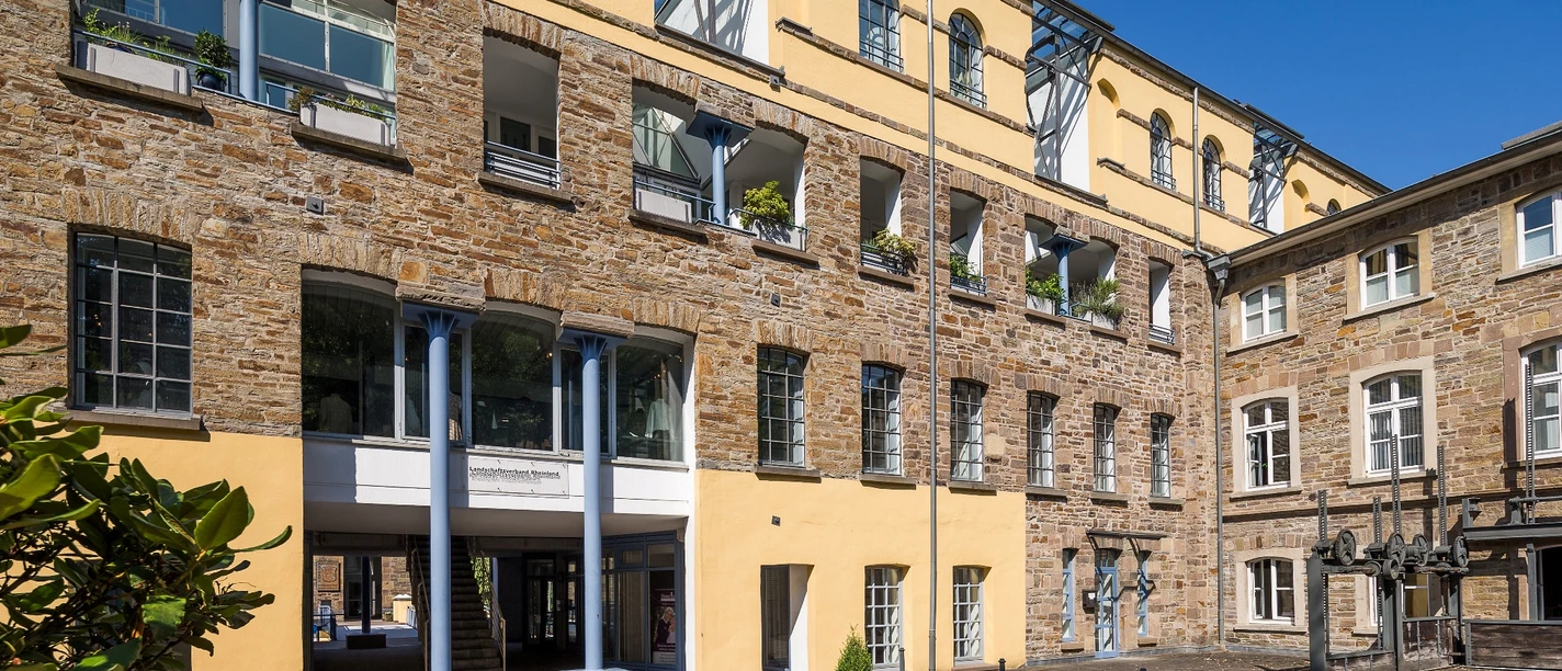 Außenansicht Kraftwerk Gelbes und steinernes Gebäude mit Arkaden, Fenstern und künstlerischen Außenskulpturen im Innenhof.