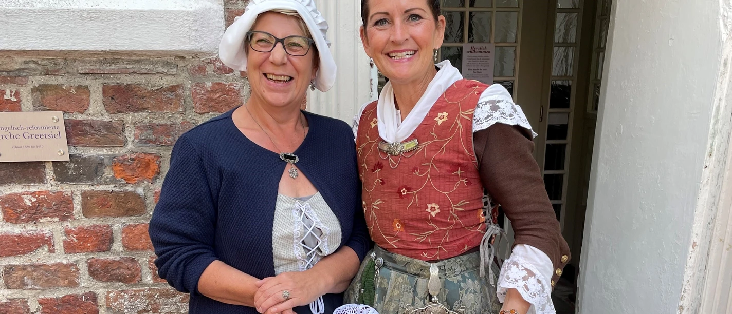 Erzähltheater mit Daje und Geeske Zwei Frauen - Daje und Geeske - in historischen Kostümen lächeln vor einem Backsteingebäude in Greetsiel.