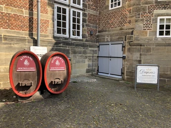 Zwei rote Eingangstüren in großen Holzfässern, nebeneinander vor einem historischen Backsteingebäude.Two red entrance doors in large wooden barrels, side by side in front of a historic brick building.To røde indgangsdøre i store trætønder, side om side foran en historisk murstensbygning.Twee rode toegangsdeuren in grote houten tonnen, naast elkaar voor een historisch bakstenen gebouw.
