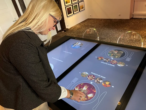 A woman operates an interactive screen in a museum with culinary exhibits.