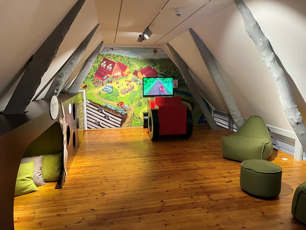Spargelmuseum Interactive exhibition in the attic with wooden floor, beanbags and a large screen.