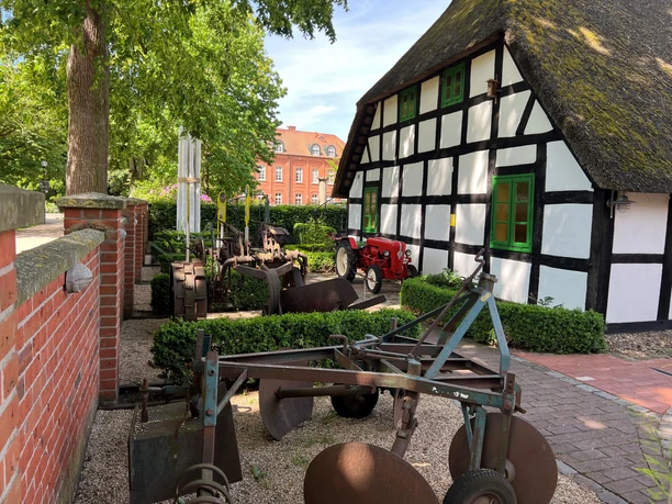 Spargelmuseum Half-timbered building with thatched roof, historic agricultural machinery and tractor in a green, rural setting.