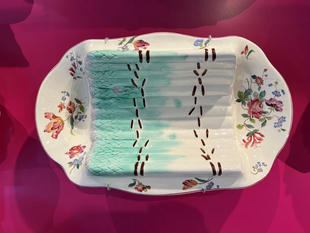 Spargelmuseum An artistically painted porcelain plate displayed on a bright pink background.