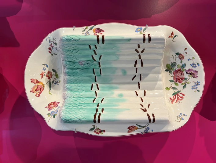Spargelmuseum Ein kunstvoll bemalter Porzellanteller ausgestellt auf einem kräftig pinkfarbenen Hintergrund.An artistically painted porcelain plate displayed on a bright pink background.En kunstnerisk malet porcelænstallerken på en lyserød baggrund.Een kunstzinnig beschilderd porseleinen bord op een felroze achtergrond.