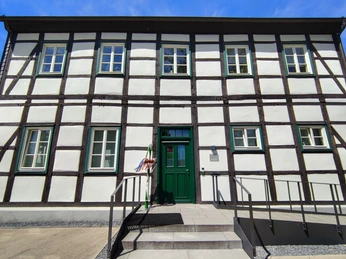 Fachwerkgebäude mit grüner Eingangstür, weißen Wänden und dunklen Holzbalken unter blauem Himmel.