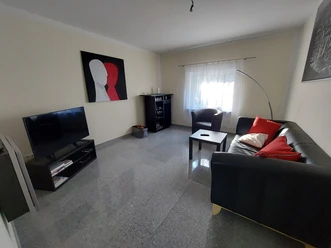 Ferienwohnung_am_Fahrenstau.jpg Helles Wohnzimmer mit Ledersofa, Flachbildfernseher, Couchtisch und modernem Kunstbild an der Wand.