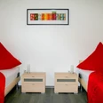 appartmentshaus_senne.jpg Zwei Einzelbetten mit roten Tagesdecken und zweckmäßigen Nachttischen in einem hellen Raum.