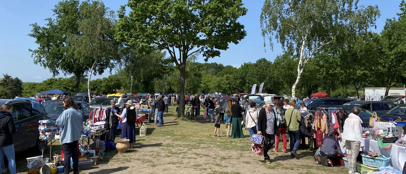 troedelmarkt-mardorf-staende.jpg Trödelmarkt in Mardorf, Besucher stöbern zwischen Verkaufsständen im Freien, umgeben von Bäumen.
