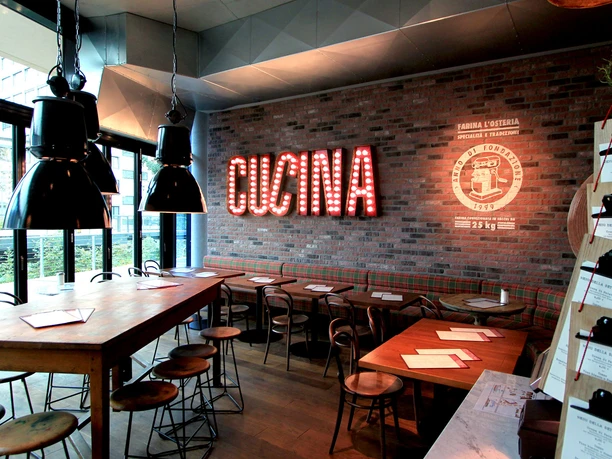 lo_osnabrueck_1_restaurantfoto_5.jpg Ein modernes Restaurant mit industriellem Dekor; Holzmöbel, Ziegelwand und große Leuchtreklame "Cucina".
