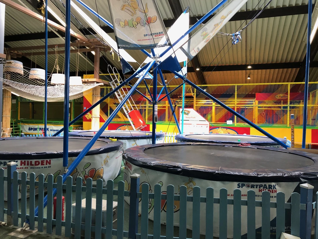 Trampolino in Hilden Große Trampoline umgeben von blauen Gittern in einer bunten Halle für sportliche Aktivitäten in Hilden.