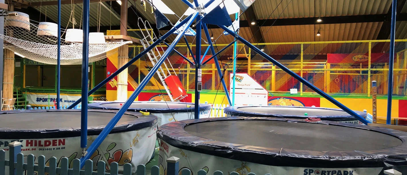 Trampolino in Hilden Große Trampoline umgeben von blauen Gittern in einer bunten Halle für sportliche Aktivitäten in Hilden.