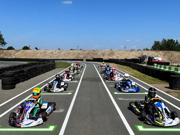 Kartbahn 1.jpg Mehrere Fahrer in Karts starten auf einer asphaltierten Rennstrecke unter blauem Himmel.