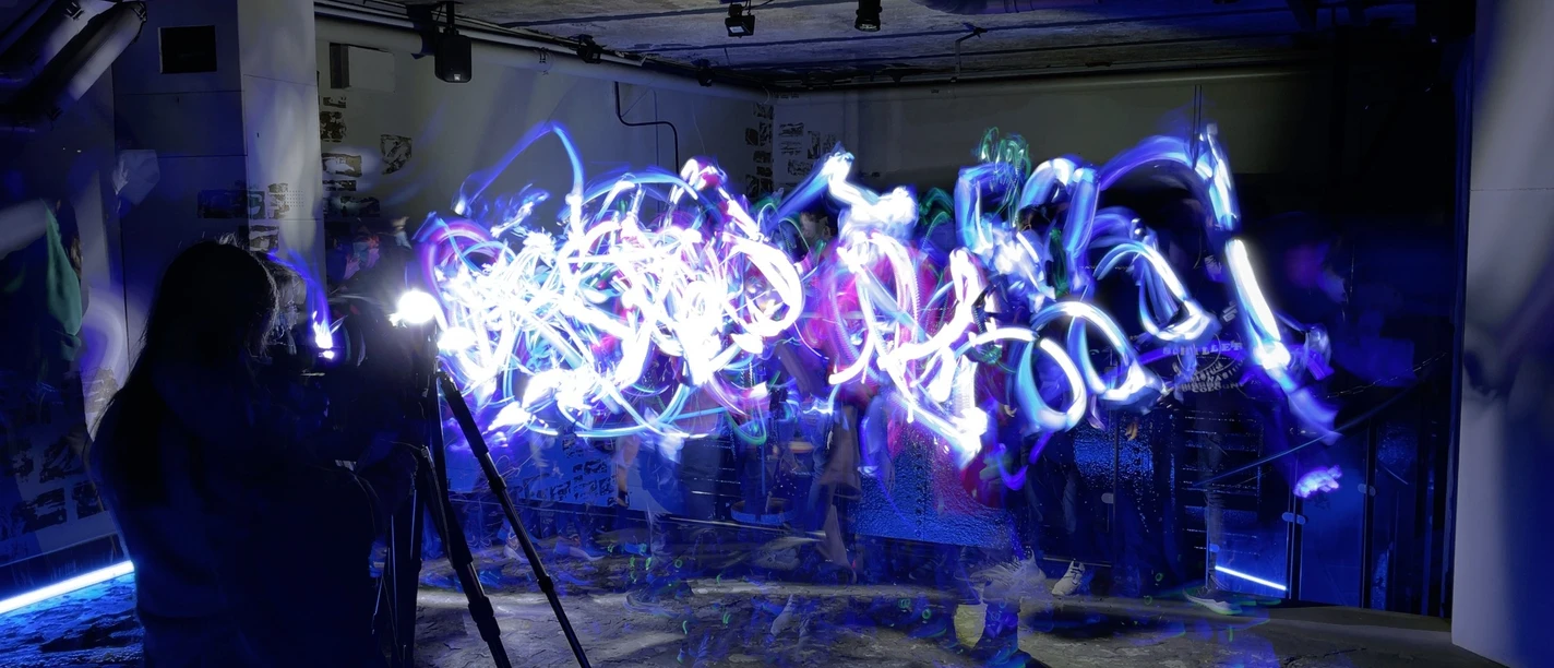 Malen mit Licht Menschen malen mit buntem Licht in dunklem, industriell aussehenden Raum mit Rohren.