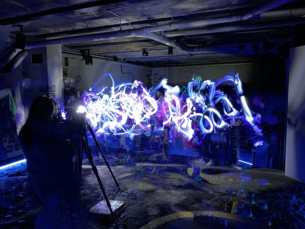 Malen mit Licht Menschen malen mit buntem Licht in dunklem, industriell aussehenden Raum mit Rohren.