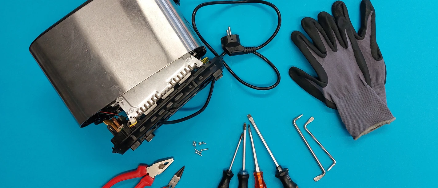 Repair Cafe andersrum Zerlegter Toaster mit Werkzeugen und Handschuhen auf blauem Hintergrund zur Reparatur bereit.