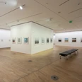 Die Photographische Sammlung/SK Stiftung Kultur Ein lichtdurchfluteter Ausstellungsraum in einer Galerie mit Holzfußboden, an dessen Wänden gerahmte Fotografien hängen.A light-flooded exhibition space in a gallery with a wooden floor and framed photographs hanging on the walls.