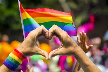 LGBTQ+ heart Hands form a heart in front of a rainbow flag