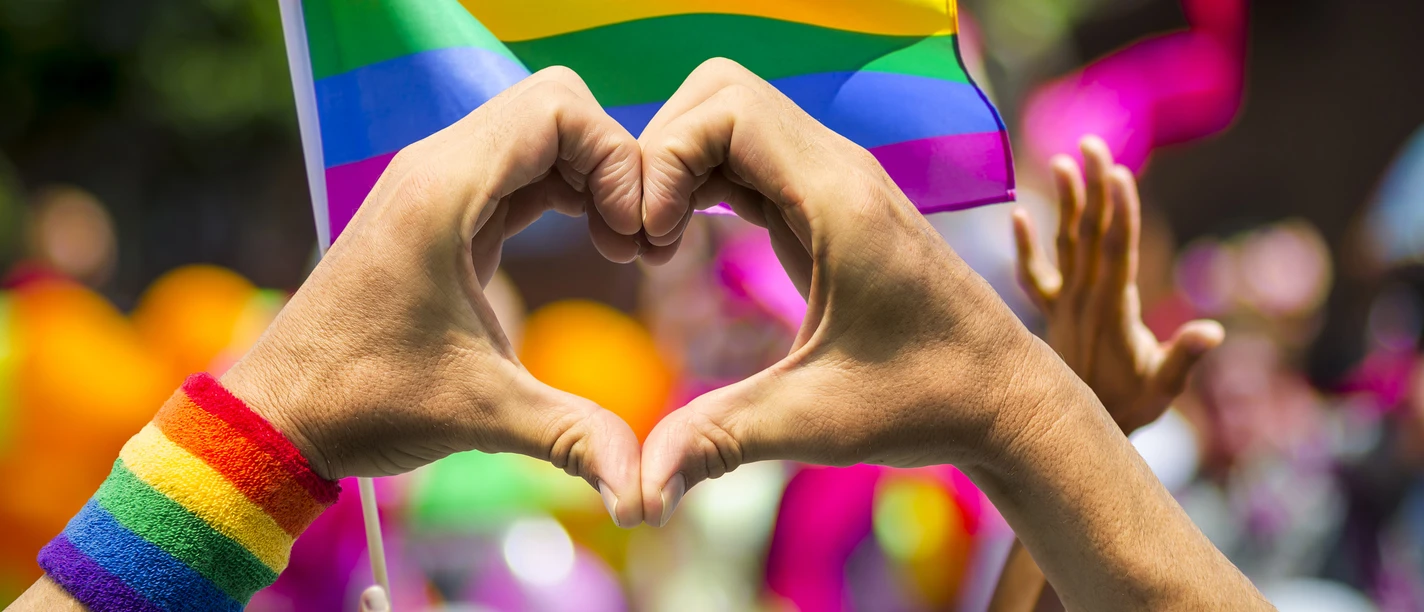 LGBTQ+ heart Hands form a heart in front of a rainbow flag