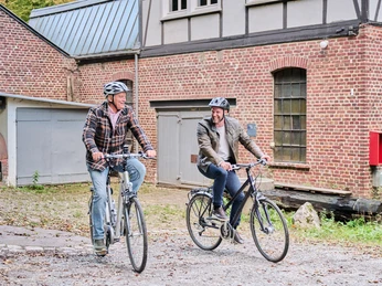Manuelskotten Zwei Personen auf Fahrrädern vor einem alten Gebäude Two people on bicycles in front of an old buildingTwee mensen op fietsen voor een oud gebouw