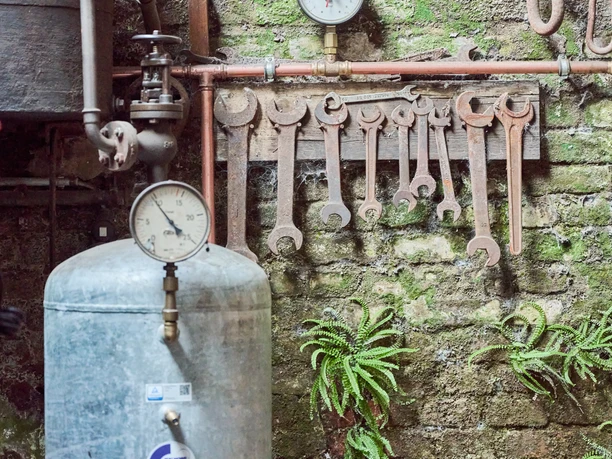 Altes Werkzeug und ein alter Boiler an einer Hausmauer