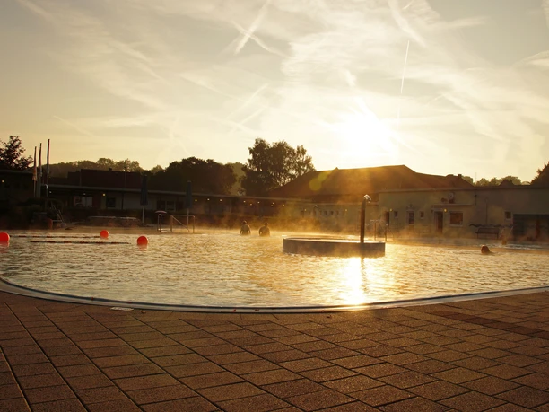 Brakel_Sommerbad_Stadt_Brakel_1 Ein beleuchtetes Freibad mit Sprüngen im Wasser und dunklen Silhouetten bei Sonnenuntergang.