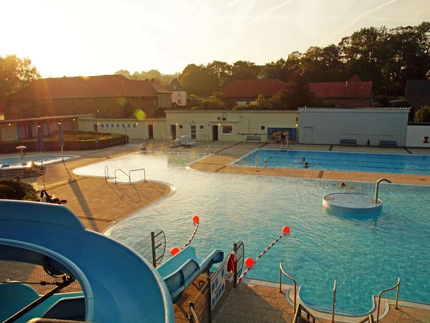 Brakel_Sommerbad_Stadt_Brakel_2 Freibad mit Kinderbereich, Rutsche und Schwimmbecken im Sonnenuntergang, umgeben von Bäumen.
