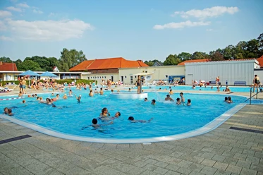 Menschen genießen sommerlichen Badespaß in einem großen Freibad mit verschiedenen Pools.
